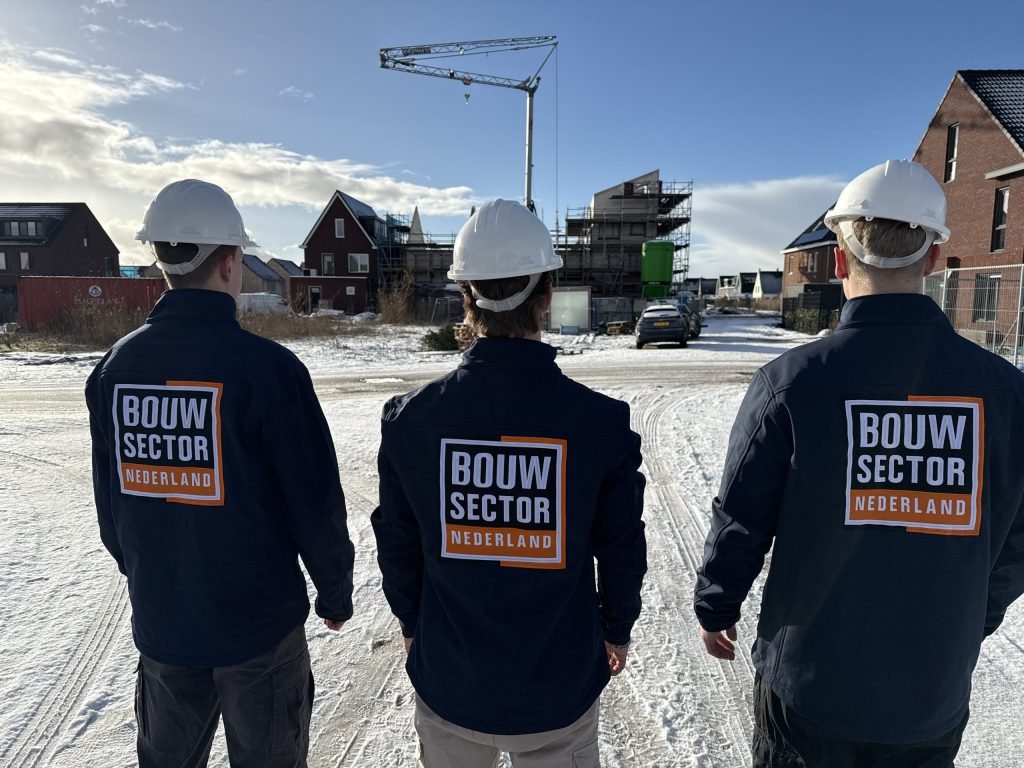 Drie vakmensen van Bouwsector Nederland met witte helm kijken naar een straat met nieuwbouwwoningen en een bouwkraan